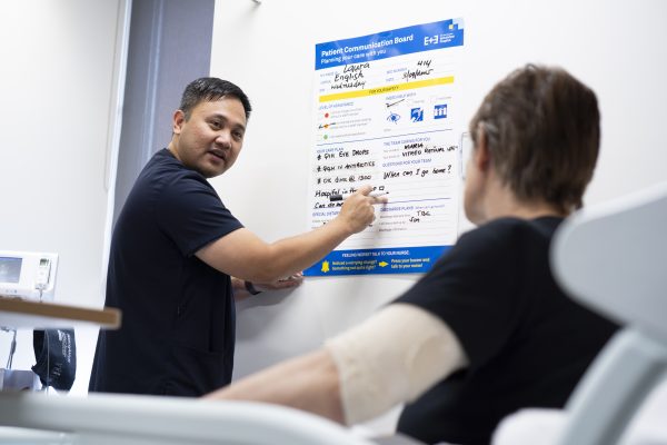 Nurse filling in patient communication board while patient looks on.