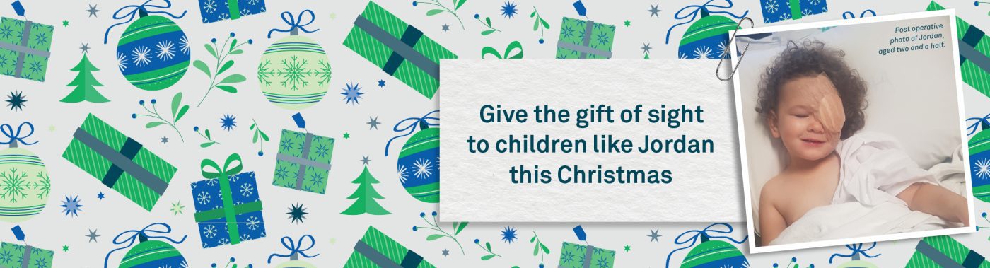 A Christmas themed banner with blue and green decorations. A photo of a young child in a hospital bed with an eye patch sits to the right hand side. Text next to the image reads 'Give the gift of sight to children like Jordan this Christmas'.