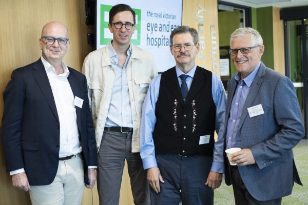 Four male Doctors standing together and smiling at the camera. The Eye and Ear logo on a TV sits in the background.