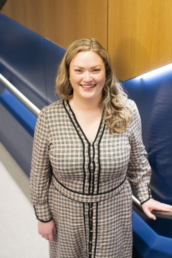 A photo of a young woman with blonde hair wearing a black and white patterned dress, smiling at the camera.