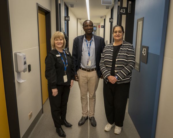 Three people standing together in a corridor of specialist clinics, smiling at the camera.