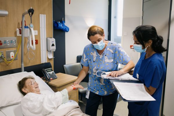 Two nurses are taking the pulse of a patient lying in a hospital bed