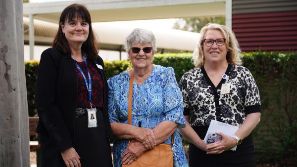 Three women standing together in an outside setting. They're all smiling fondly at the camera.