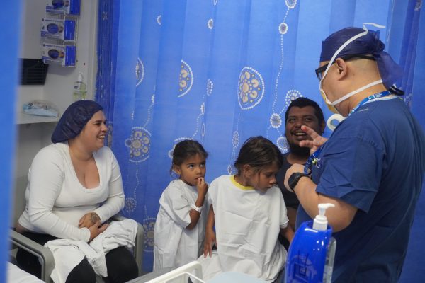 Brittany, Adurey, Diane and their dad Andrew laughing at what a anaesthetist in blue scrubs and a mask is saying whilst sitting down in a preadmission bay.