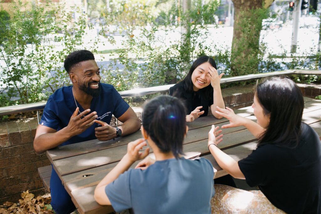 Four people sitting around a table outside, smiling in conversation.